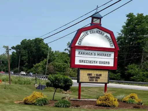 The sign for Carlisle Country Market shows where local shops and markets are. Mid State Baths, known for installing showers, is nearby in a quiet area with plants and trees around it. Alt text: Carlisle Country Market sign near Mid State Baths, a trusted bathroom remodeler.