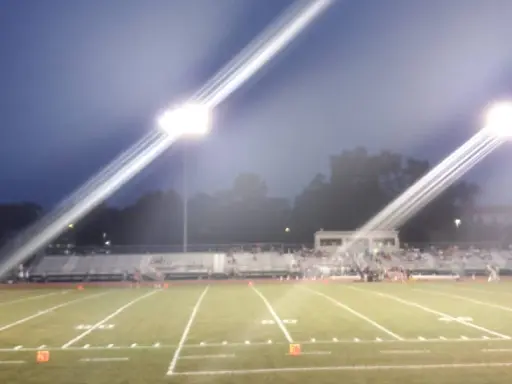 Mid State Baths banners appear by a football field during an evening game, showing community involvement in York, PA.